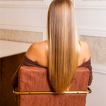 Woman with long blonde hair sitting on a brown chair in an elegant room.