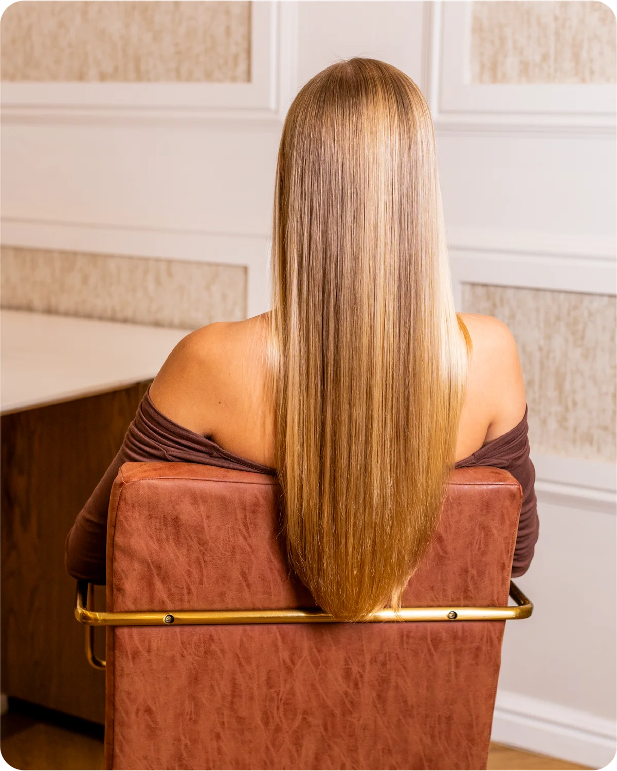 Woman with long blonde hair sitting on a brown chair in an elegant room.