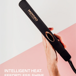 Black hair straightener with 'Moyoko' branding held by a hand on a pink and white background.