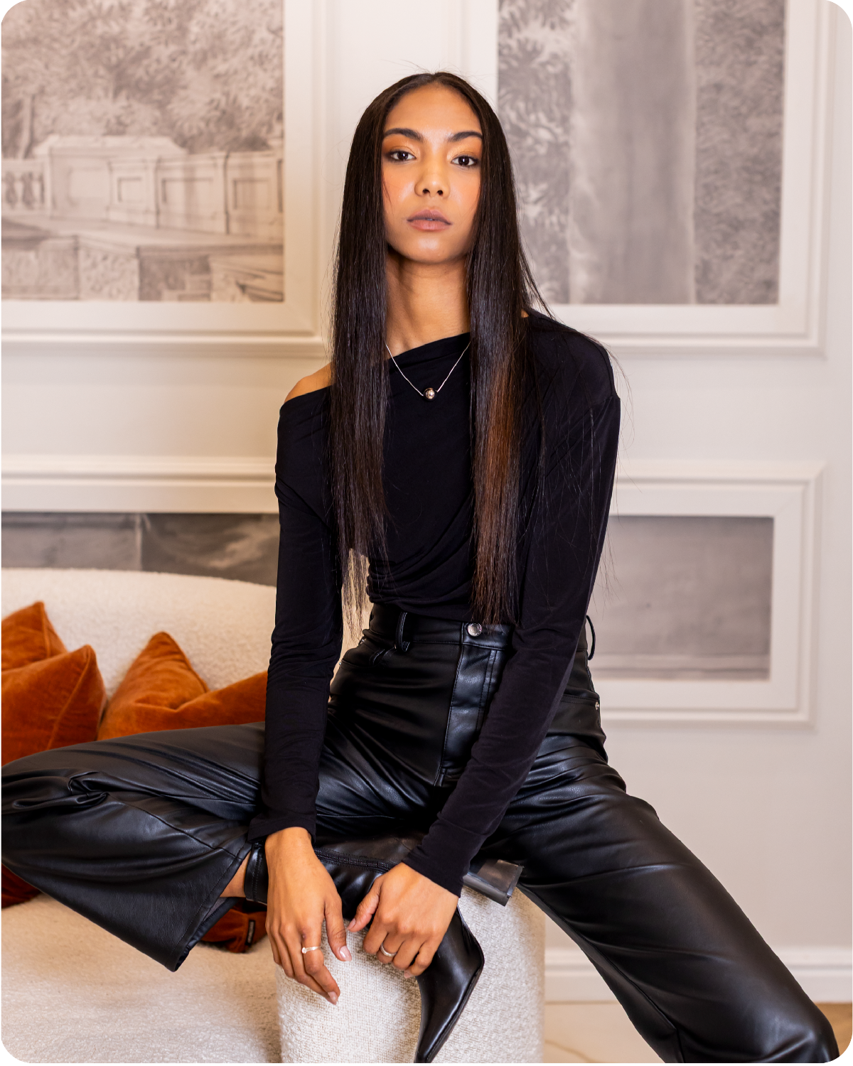 Woman in black outfit sitting on a couch in a stylish room. Her hair is perfect . 