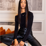 Woman in black outfit sitting on a couch in a stylish room.