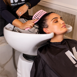 Woman getting her hair washed at a salon with a stylist using a pink OG comb.
