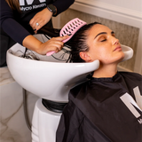 Woman getting her hair washed at a salon with a stylist using a pink OG comb.