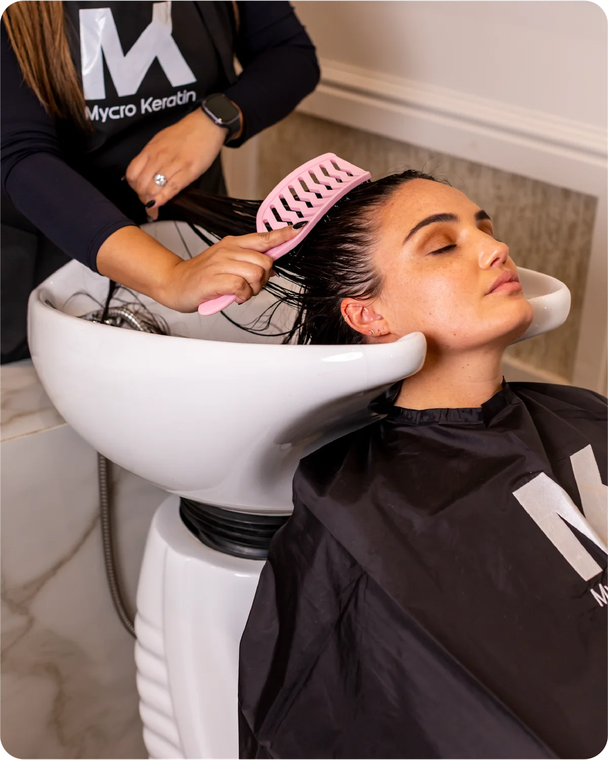 Woman getting her hair washed at a salon with a stylist using a pink OG comb.