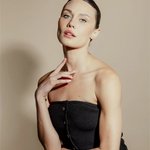 Woman wearing a black strapless dress against a beige background. Her hair is perfectly pulled back. 