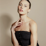 Woman wearing a black strapless dress against a beige background. Her hair is perfectly pulled back. 