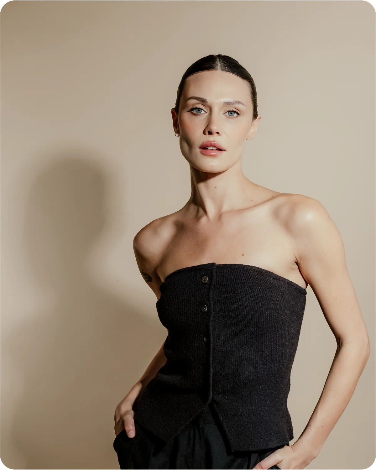 Woman wearing a black strapless top against a beige background. Her hair is perfectly pulled back and no flyways as she uses Sleek back hair wax stick